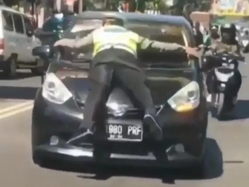 Brigadir natan Doris merelakan tubuhnya nempel di kap sebua mobil yang melanggarn lalu lintas di jalan Pasirkaliki, Kota bandung (Foto: okezone)