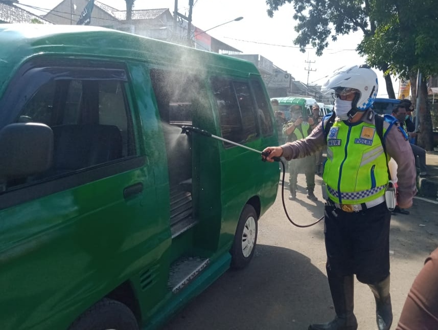 Seorang anggota Polsek Cicalengka melakukan penyemprotan disinfektan ke salah satu angkot yang melintas di kawasan Alun-alun Cicalengka, Kabupaten Bandung, Jawa Barat, Selasa (7/4/2020). (Foto: Muhammad Zein/dara.co.id)