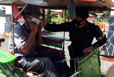 Seorang anggota Batalyon B Brimob Polda Jabar memasangkan masker kepada seorang kusir delman di kawasan Cipanas, Kabupaten Cianjur, Jawa Barat, Kamis (7/5/2020). (Foto: Angga Purwanda/dara.co.id)